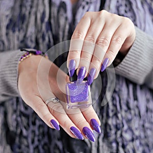 Female hand with purple lilac manicure holds a bottle of nail polish