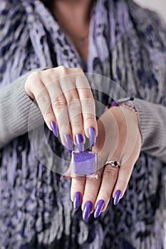 Female hand with purple lilac manicure holds a bottle of nail polish