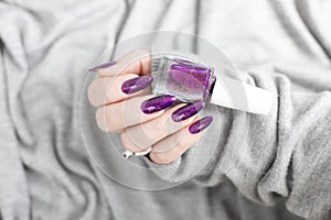 Female hand with purple lilac manicure holds a bottle of nail polish