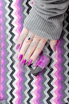 Female hand with purple lilac manicure holds a bottle of nail polish