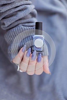Female hand with purple lilac manicure holds a bottle of nail polish