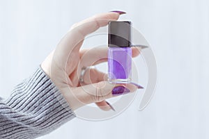 Female hand with purple lilac manicure holds a bottle of nail polish