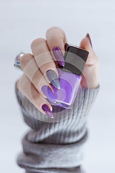 Female hand with purple lilac manicure holds a bottle of nail polish