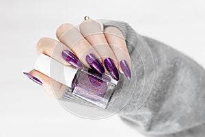 Female hand with purple lilac manicure holds a bottle of nail polish