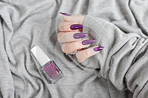 Female hand with purple lilac manicure holds a bottle of nail polish