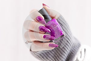 Female hand with purple lilac manicure holds a bottle of nail polish