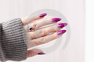 Female hand with purple lilac manicure holds a bottle of nail polish