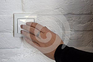 Female hand pushes button of white Switch on brick wall. Close-up. Copy space