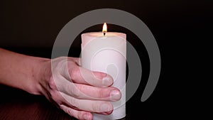 Female Hand Puts a Burning White Candle on the Table in a Dark Room. Close up