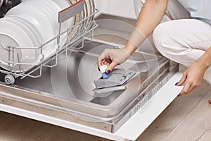 female hand puts dishwasher tablet into open dishwasher machine