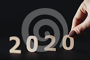 Female hand puts numbers symbolizing the coming of the new 2020 year instead of the old 2019, wooden figures on black background,