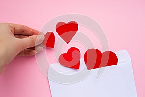 Female hand puts paper red hearts in a white envelope. Love letter. Valentine`s day concept. Happy Valentine's day photo