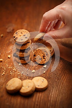 Female hand puts small bisqiut cookies on each other with chocolate pieces between and makes turret at wooden table background wi
