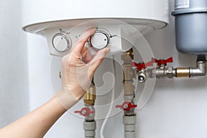 Female hand puts thermostat of electric water heater boiler in a high power consumption mode