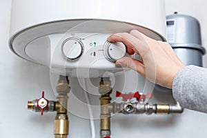 Female hand puts thermostat of electric water heater boiler in low low power consumption mode