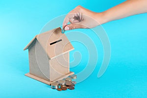 A female hand putting a coin into a money box. The concept of financial savings to buy a house.