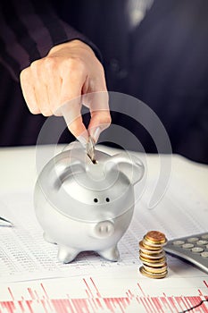 Female hand putting coin in piggy bank on the office desk