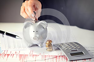 Female hand putting coin in piggy bank on the office desk