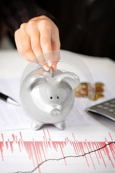 Female hand putting coin in piggy bank on the office desk