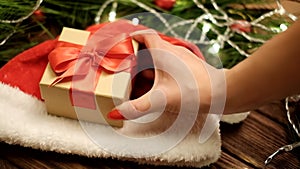 Female hand putting a gift box on Santa hat.