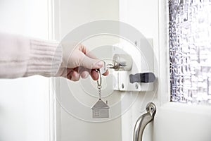 female hand putting house key into front door lock of house, Woman using a silver key to open lock of the front door
