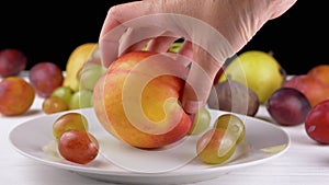 Female Hand Putting a Ripe Apple or Peach on a Plate with Grape and Fruit