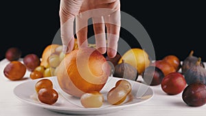 Female Hand Putting a Ripe Apple or Peach on a Plate with Grape and Fruit