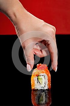 Female hand reaching out to Philadelphia sushi roll with salmon, cream cheese, avocado and red caviar