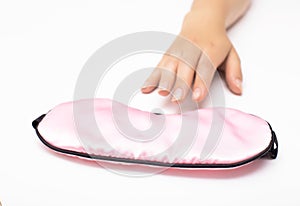 Female hand reaching for a pink sleep mask on a white background, concept of anxious sleep and insomnia, close-up, sleeplessness