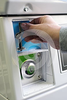 A female hand ready to insert a token into the slot of a vintage chrome coin receptacle mounted on the washing machine.