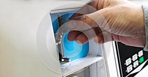 A female hand ready to insert a token into the slot of a vintage chrome coin receptacle mounted on the washing machine.