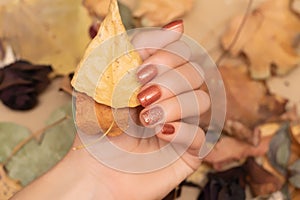 Female hand with red autumn nail design. Woman hand hold dry leaves. Red autumn nail polish manicure with golden glitter