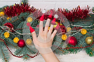 Female hand with red Christmas hats on the fingers with hats with buboes against the background of a Christmas tree with photo