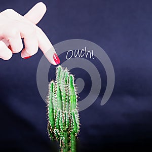Female hand with red manicure and green cactus. Ouch. Danger concept. Black background