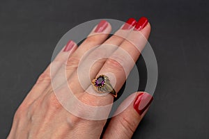 Female hand with red manicure holding golden ring on black background