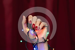 Female hand with red nail design. Glitter red nail polish manicure. Woman hand hold Christmas garland on red background