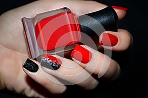 Female hand with red nail design holding nail polish bottle