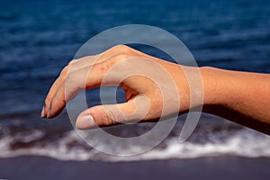 Female hand with red sunburn skin on blue sea background. Sun burned skin peeling. Seaside threat