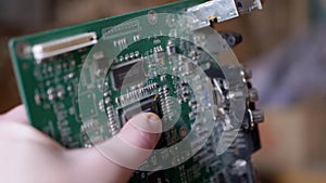 Female Hand Rotates Old Printed Circuit Board with Chip, with Conductive Tracks