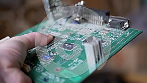 Female Hand Rotates Old Printed Circuit Board with Chip, with Conductive Tracks