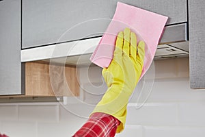 Female hand in rubber protective yellow gloves cleaning the kitchen metal extractor hood with rag. Housekeeping concept