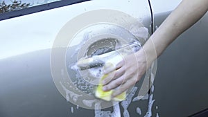 Female hand rubbing the car door handle with foam with yellow sponge.