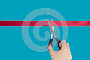 Female Hand scissors cuts a red ribbon. Isolate on a blue background