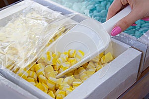 Female hand with a scoop is picking up yellow candy from a cardboard box. details of candy at the candy shop