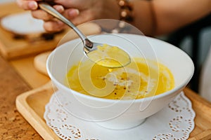 Female Hand Scooping Classic Pureed Pumpkin Soup topping with Milk, Cream and Pepper with silver spoon