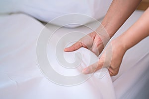 Female Hand set up white bed sheet in bedroom or maid hands making bed in a hotel room