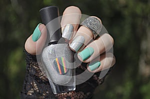 Female hand with short nails and turquoise gray holographic manicure holds a bottle of nail polish