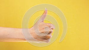 Female hand show thumbs up gesture. Woman hand rise OK good sign closeup isolated at yellow screen background