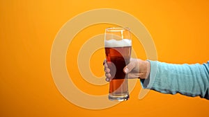 Female hand showing beer glass on yellow background, inviting customers to pub