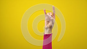 Female hand shows the sign of the horns. Studio photography on an isolated yellow background.